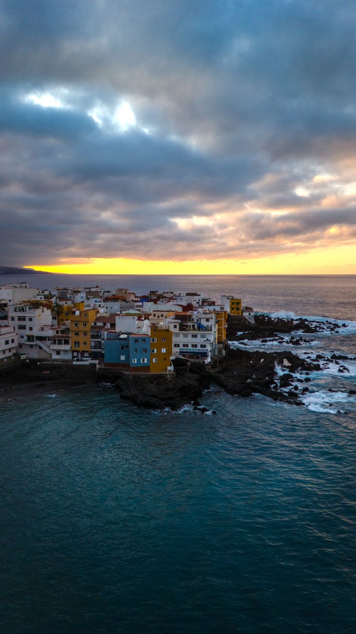 A stunning aerial view of the colorful buildings along the Puerto de la Cruz coastline at sunset in Tenerife, Spain.