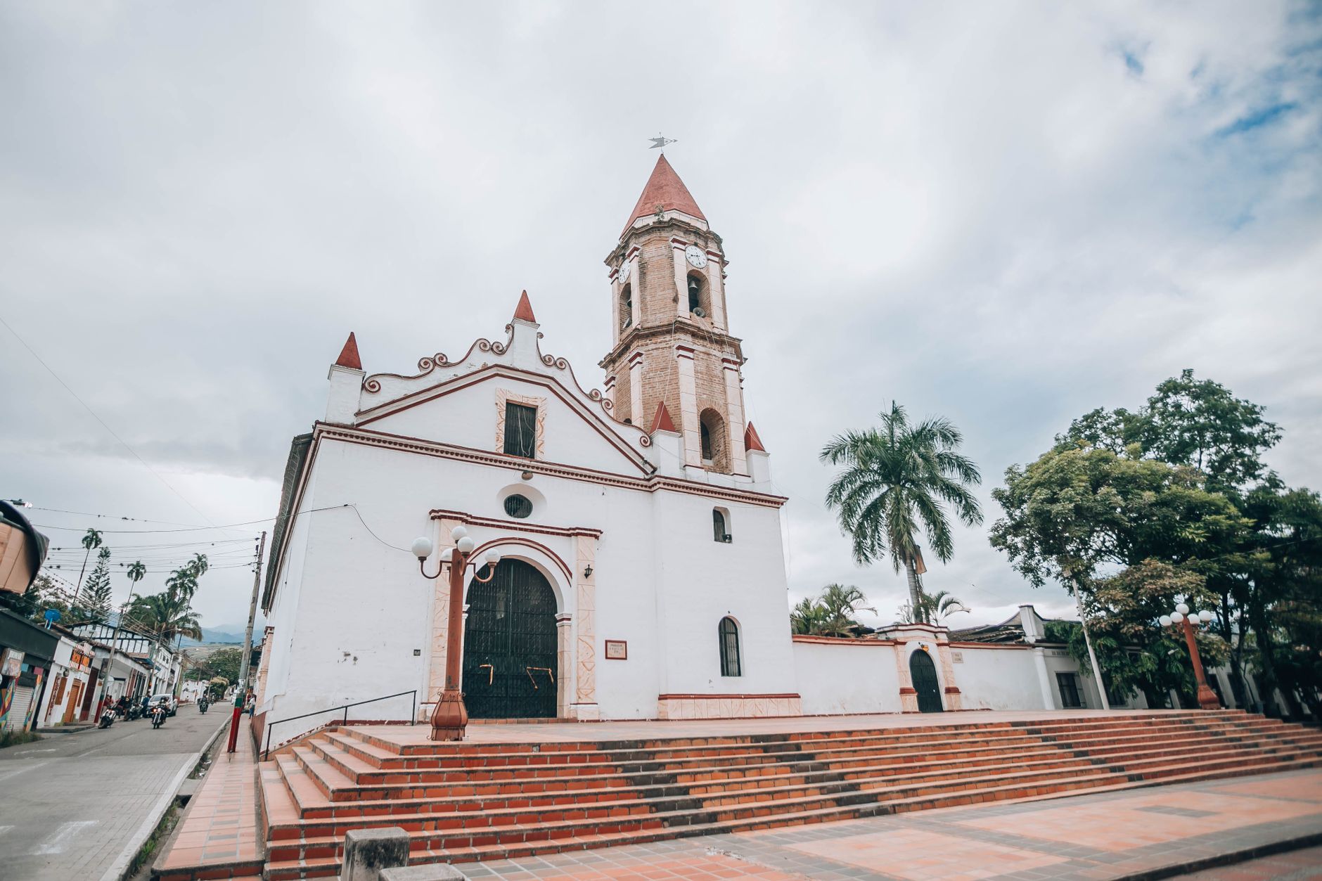 A charming rustic white church with a tall red-roofed tower and steps leading up to the entrance.